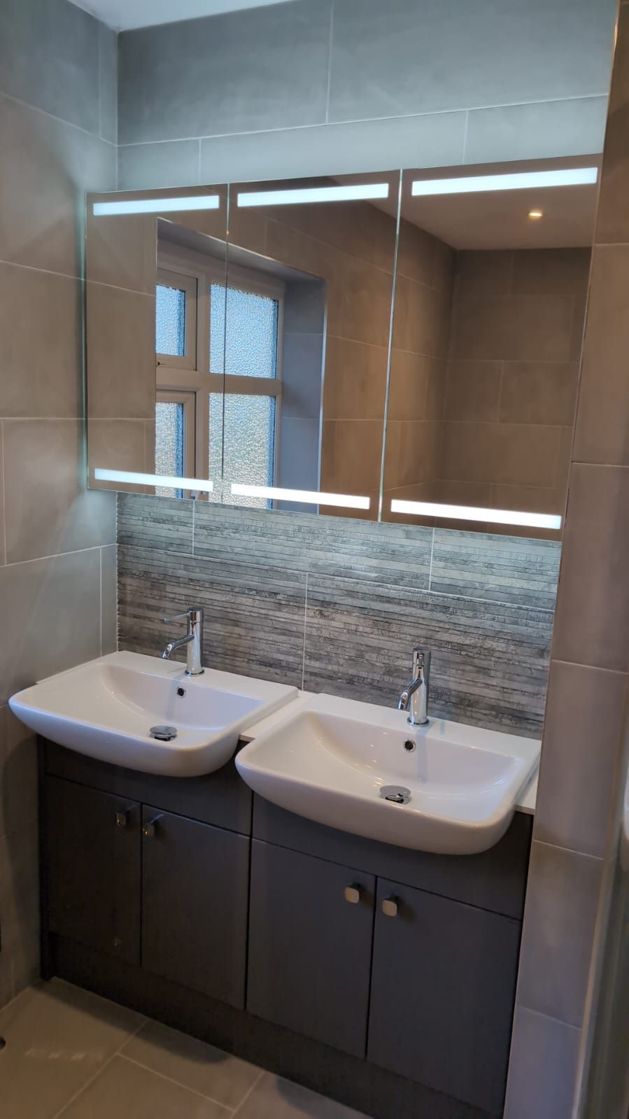Double basin vanity unit with illuminated mirrored cabinets, grey furniture and textured grey feature tiles