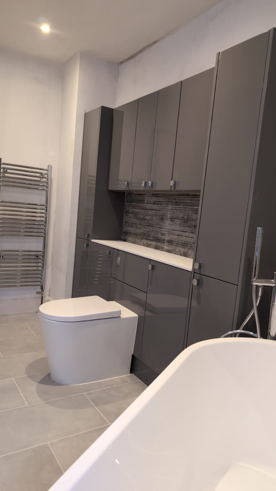 Finished bathroom with grey storage furniture, concealed cistern WC, chrome towel radiator and freestanding bath