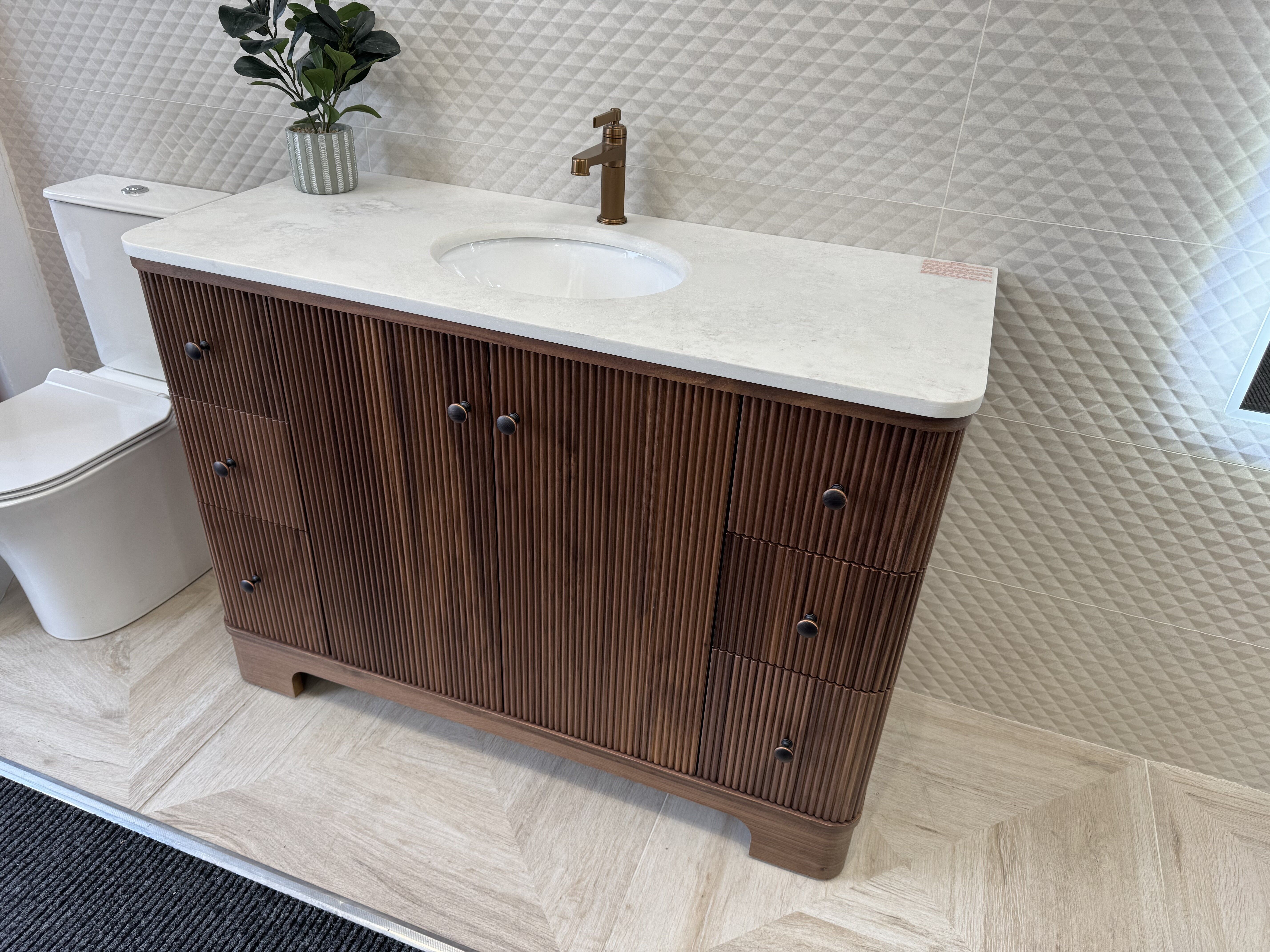 Close-up of the Hayward Walnut vanity unit showing the fluted wood finish, white basin and brushed bronze details.
