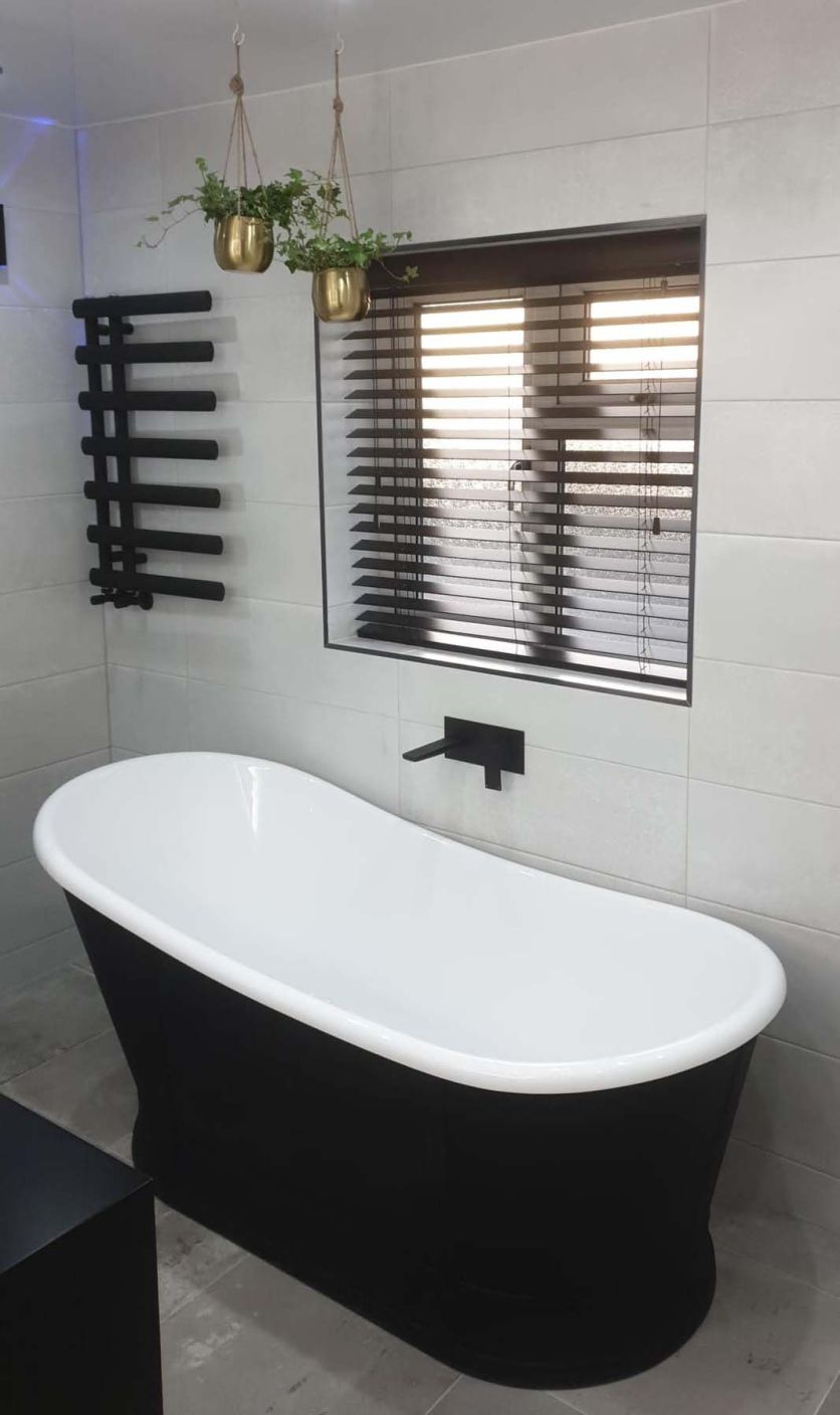 Modern bathroom with black freestanding bath, grey tiles, matt black bath filler and designer towel rail.