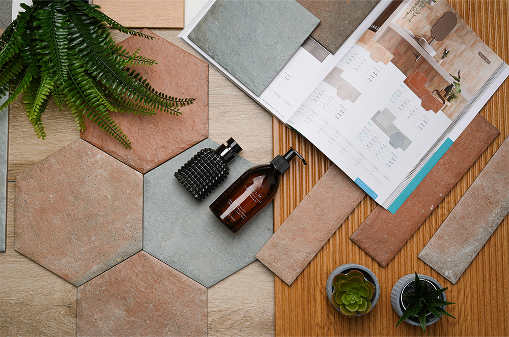 Bathroom tile mood board featuring terracotta hexagon and brick tiles, grey tile samples, wood-effect finishes, plants and an open tile brochure.