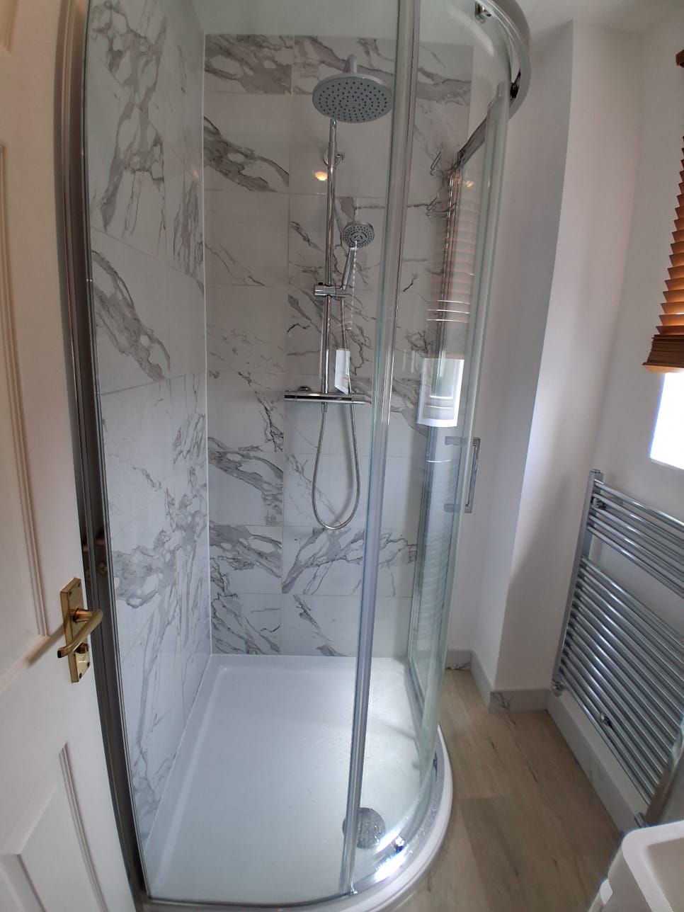 Corner shower enclosure with chrome fittings and marble-effect wall panels in a compact bathroom renovation.Corner shower enclosure with chrome fittings and marble-effect wall panels in a compact bathroom renovation.