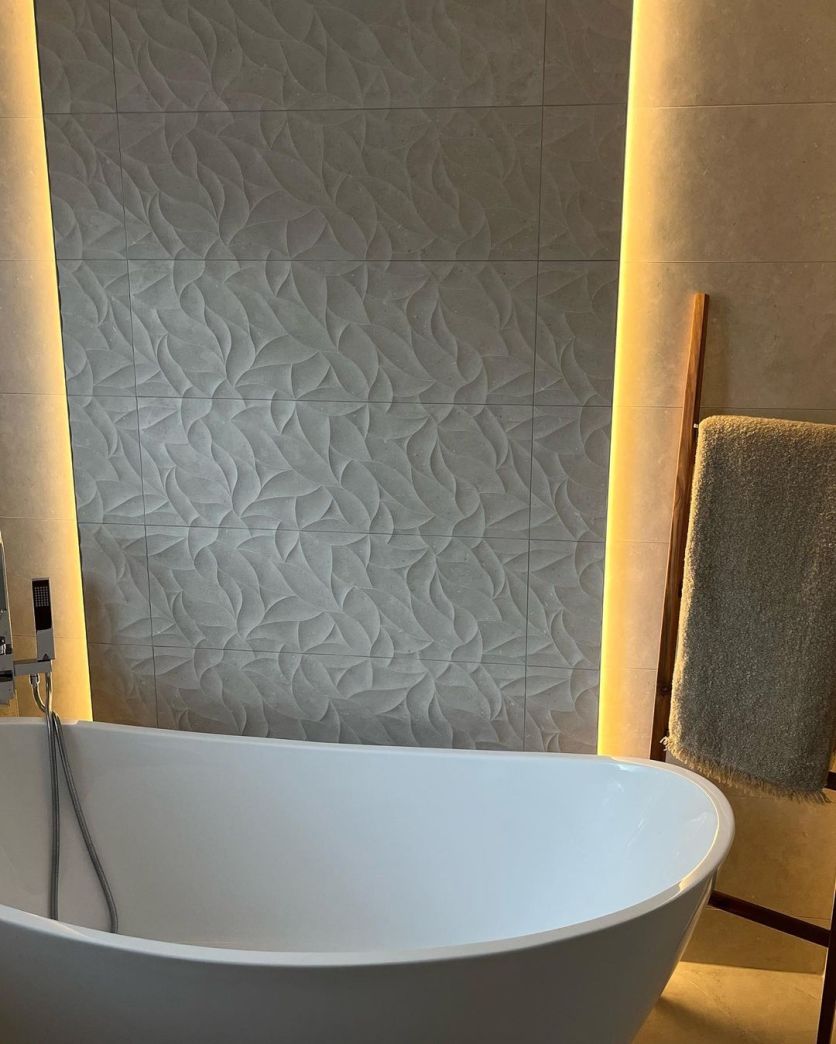 Modern spa-style bathroom with grey textured feature wall, warm LED lighting and a white freestanding bath.