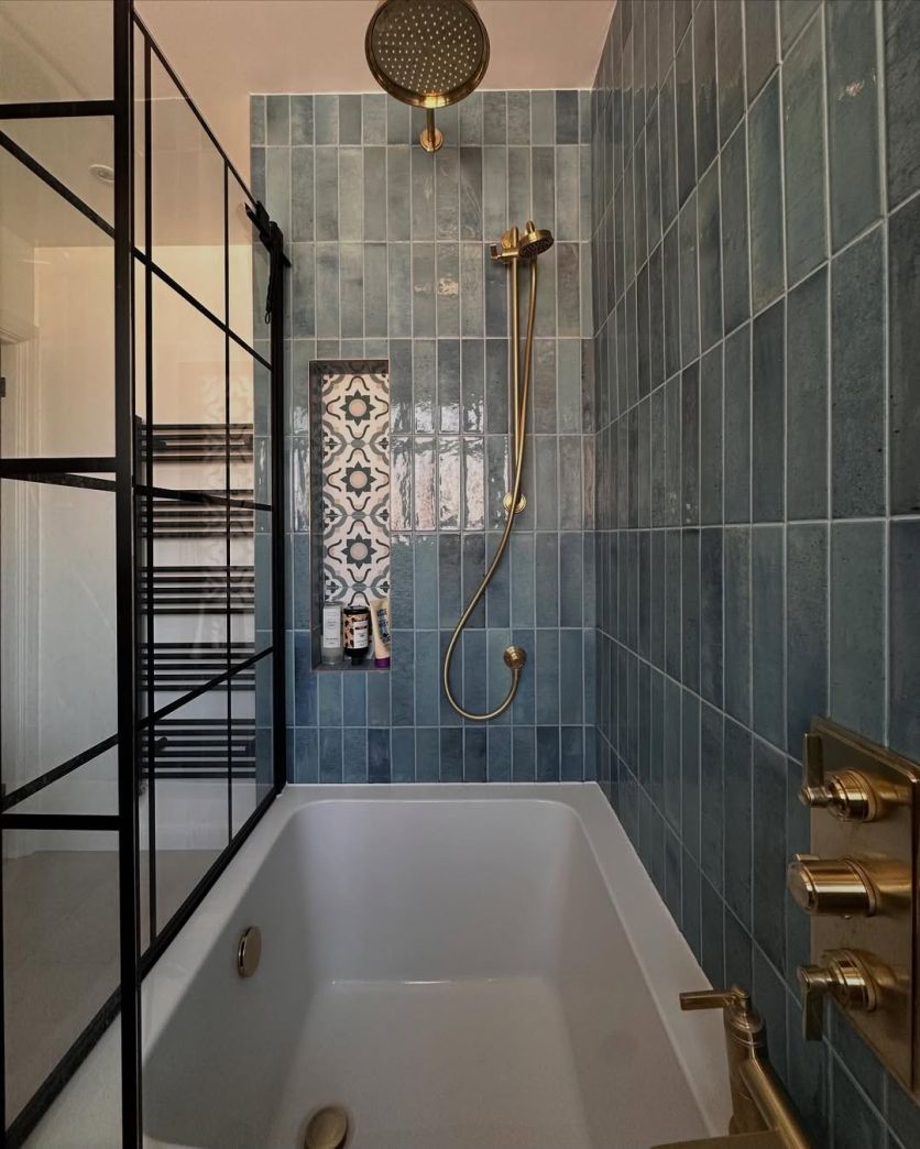 A stylish shower-over-bath featuring vertical teal gloss brick tiles, a Downton brushed gold rainfall shower and valve, and an Amien matt black grid-framed bath screen.