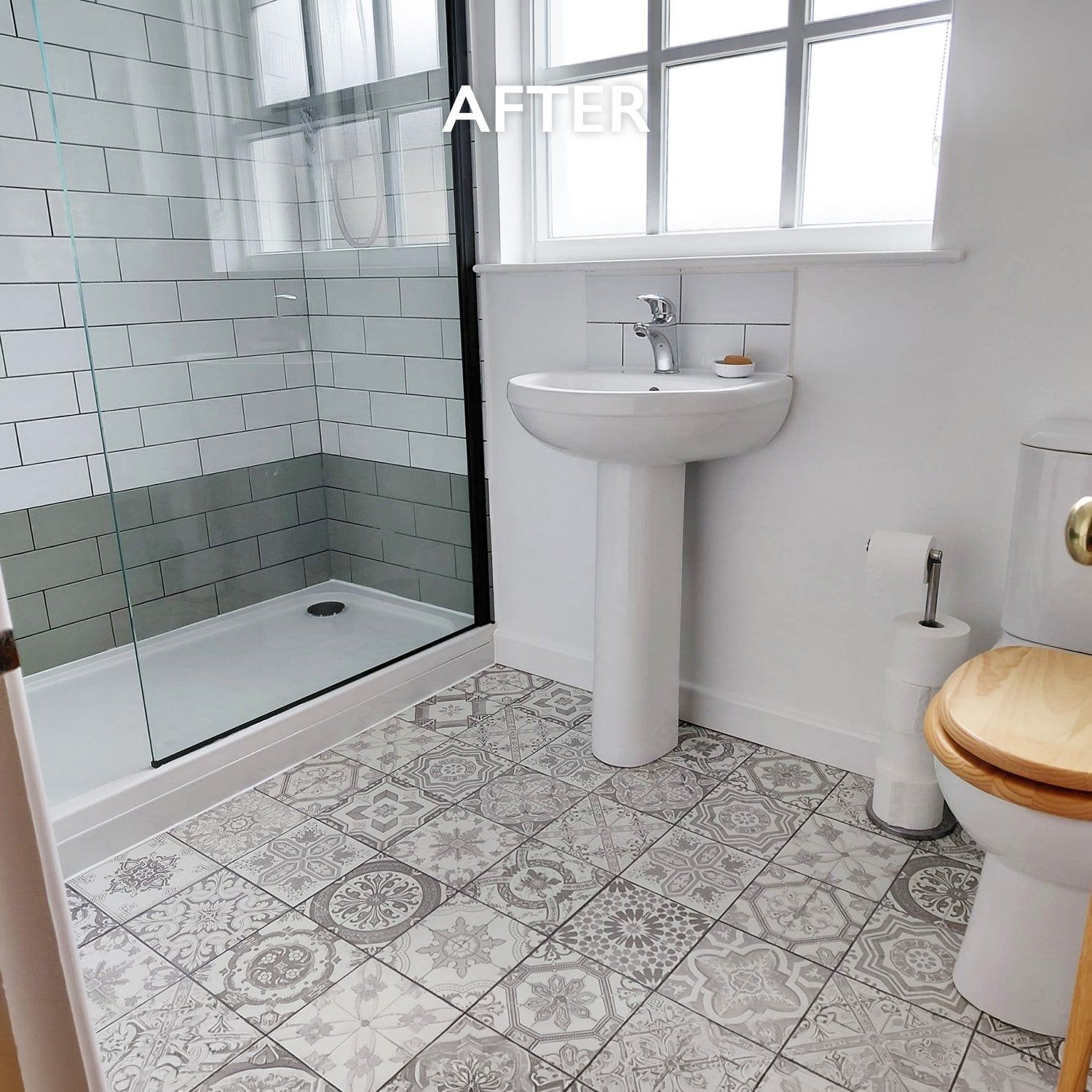After photo of a refreshed bathroom with patterned floor tiles, white metro wall tiles, a grey tiled shower area, pedestal basin and toilet.