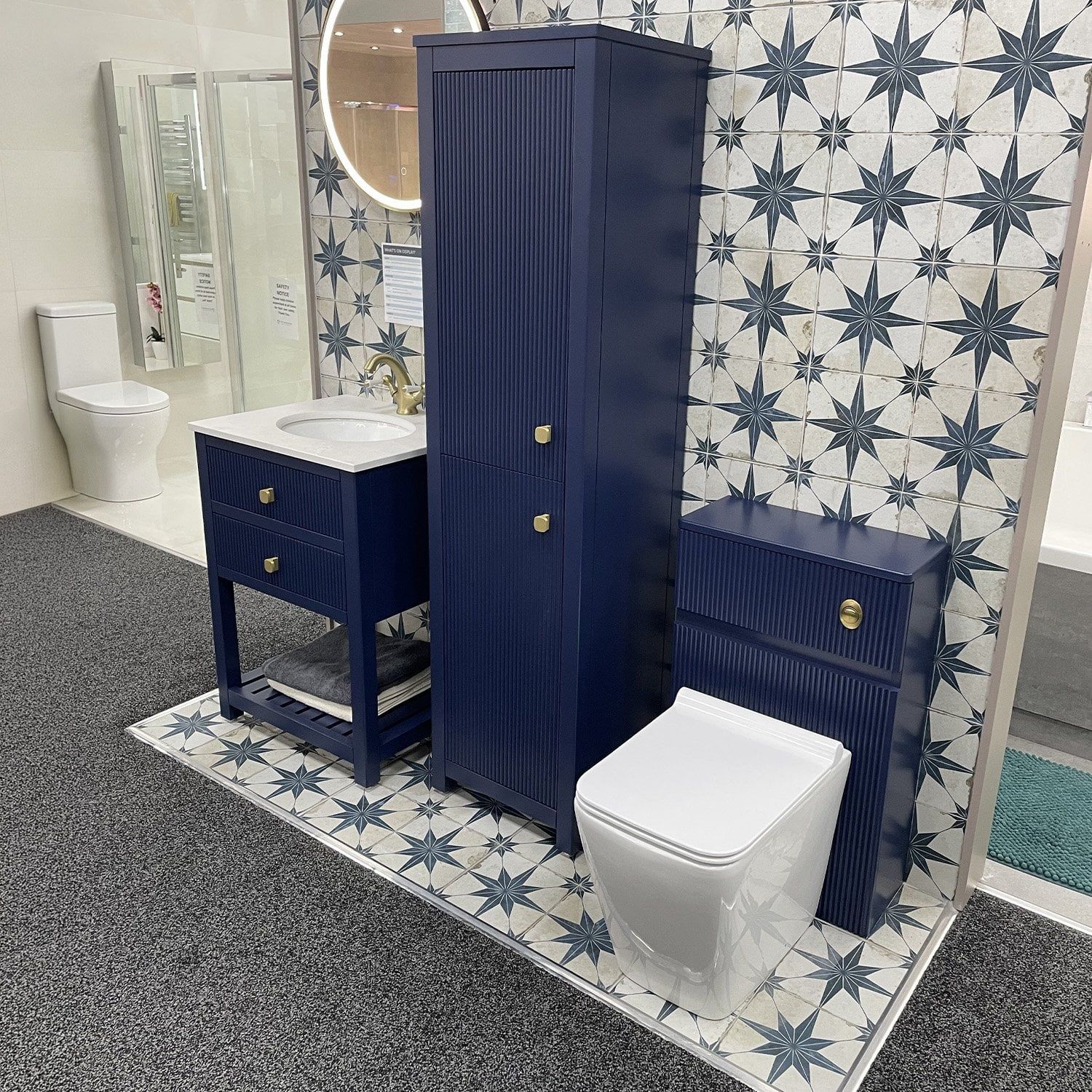 Navy ribbed bathroom furniture display with a vanity unit, tall storage cabinet, matching WC unit, brass handles and patterned tiles.