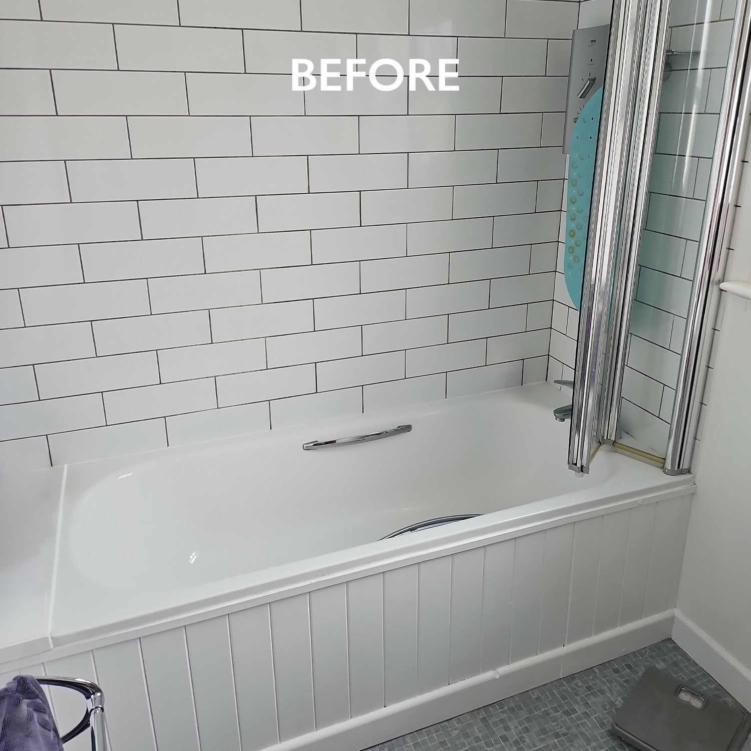 Before photo of the original bathroom with a fitted bath, folding shower screen, white metro wall tiles and grey mosaic flooring.