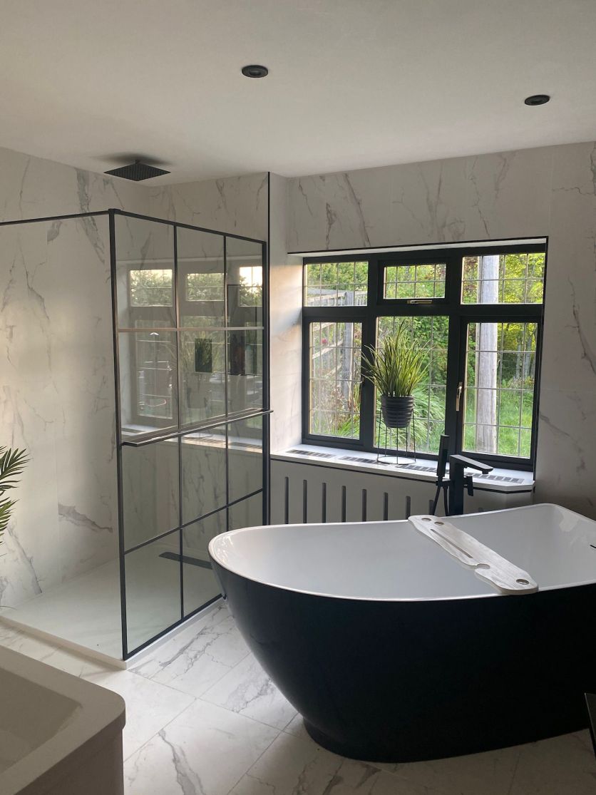 Luxury modern bathroom with black freestanding bath, marble-effect walls and flooring, black framed shower enclosure and matt black fixtures.