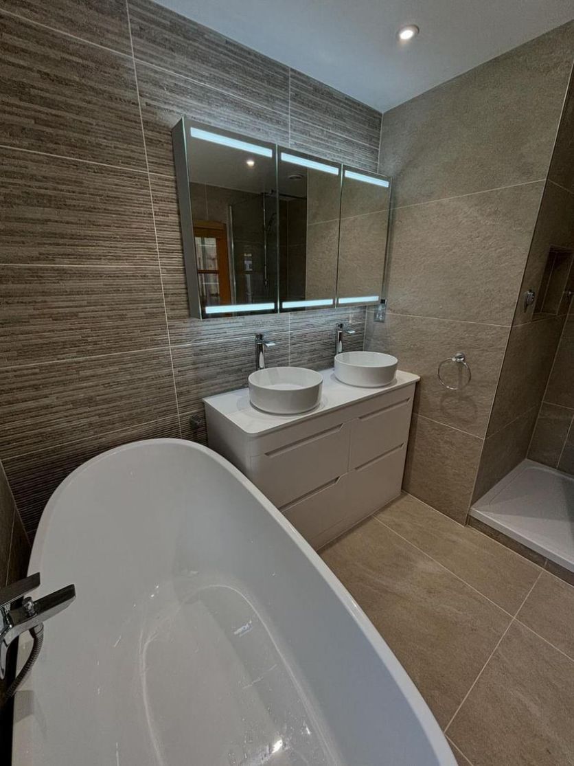 A serene spa-style bathroom featuring an Isleworth freestanding slipper bath, an Ellis 1200mm matt white double vanity with twin Damon basins, and a Corton motion sensor LED mirrored cabinet against a textured linear feature wall.