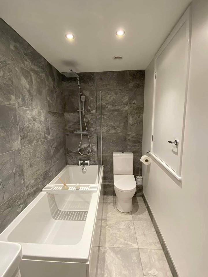 Modern bathroom with grey stone tiles, white single-ended bath and chrome shower fixtures.
