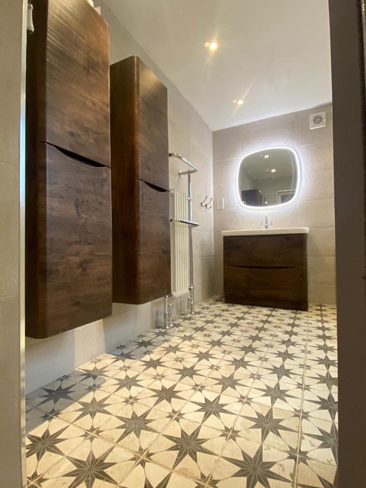 Bathroom with star-patterned floor tiles, rosewood storage cabinets, chrome towel rail and an LED mirror above a matching vanity.