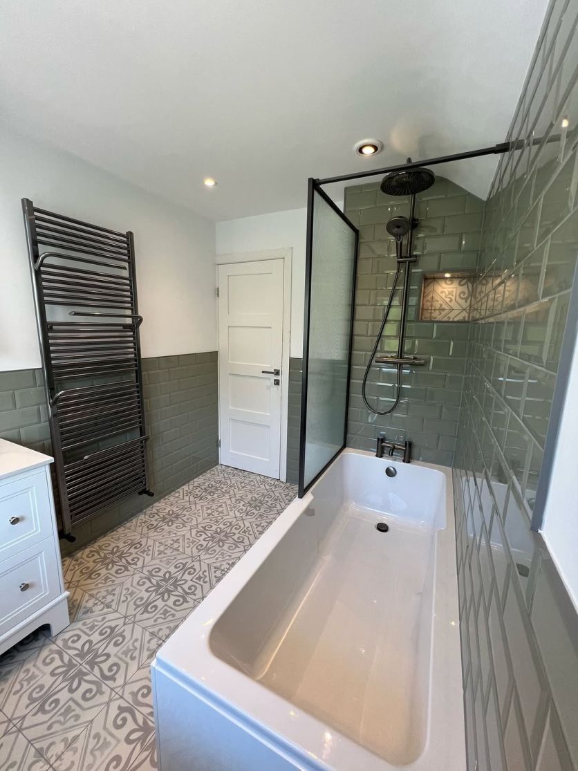 A modern-traditional bathroom featuring Sage green metro wall tiles, Xabia silver patterned floor tiles, and an Amien gunmetal framed fluted glass bath screen over a Jorden compact shower bath.