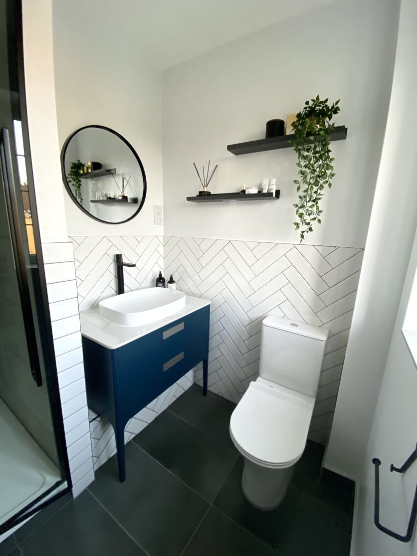 A contemporary ensuite featuring a deep blue floor-standing vanity unit with a white vessel basin and matt black tall mixer tap, set against white herringbone wall tiles and dark grey floor slabs.