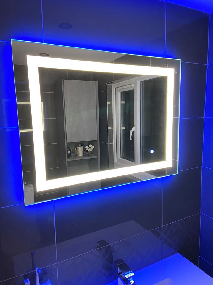 A large rectangular landscape LED bathroom mirror with a frosted light border and vibrant blue ambient backlighting, mounted on sleek charcoal grey gloss wall tiles.