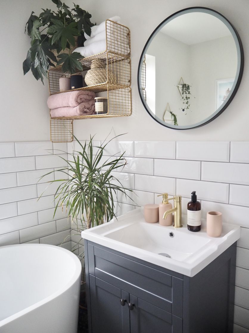 Traditional cottage-style bathroom with white metro tiles, grey vanity, round black mirror and warm gold tap accents.