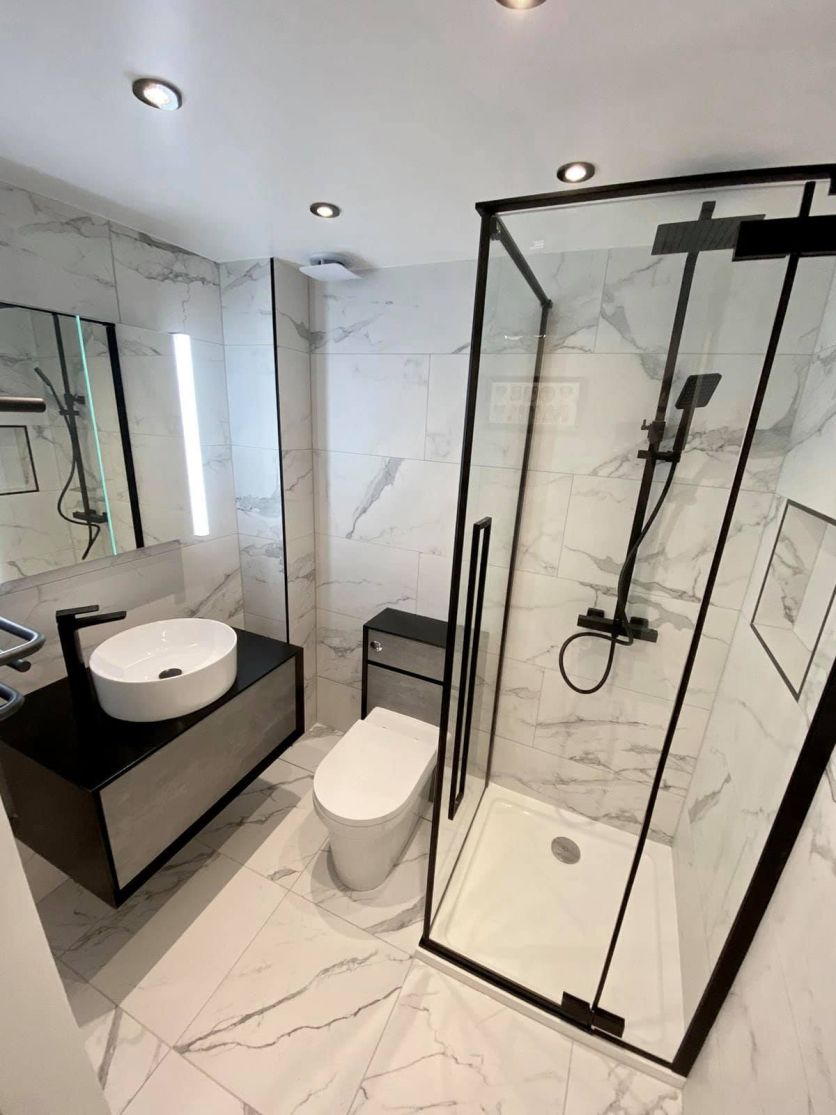 Modern bathroom with marble tiles, black-framed shower, wall-hung vanity and round countertop basin with matt black fittings.