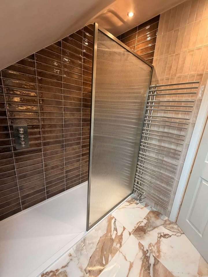 Stunning fluted glass shower screen and luxurious chrome radiator paired with elegant brown glossy wall tiles.