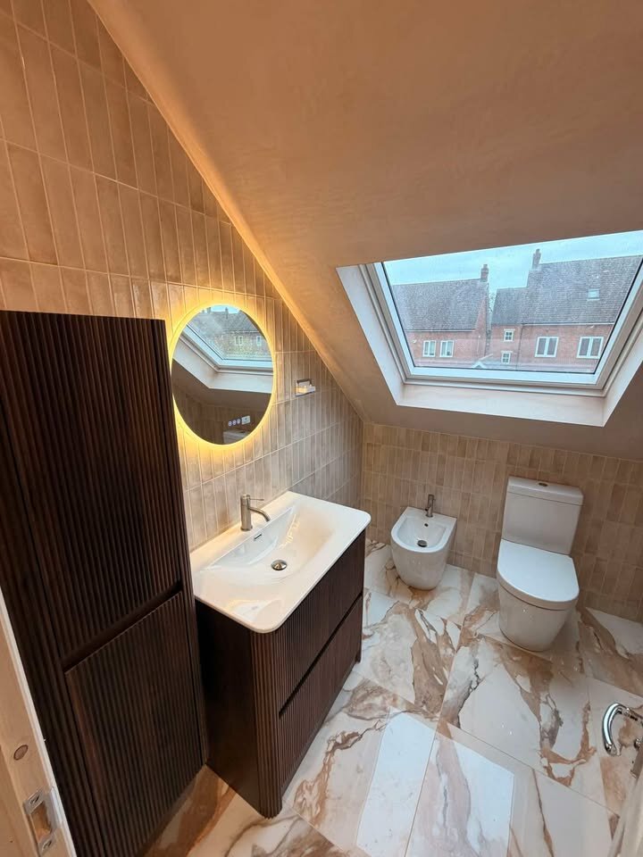 Stunning fluted walnut vanity and elegant backlit mirror beside a sleek toilet on luxurious veined marble flooring.