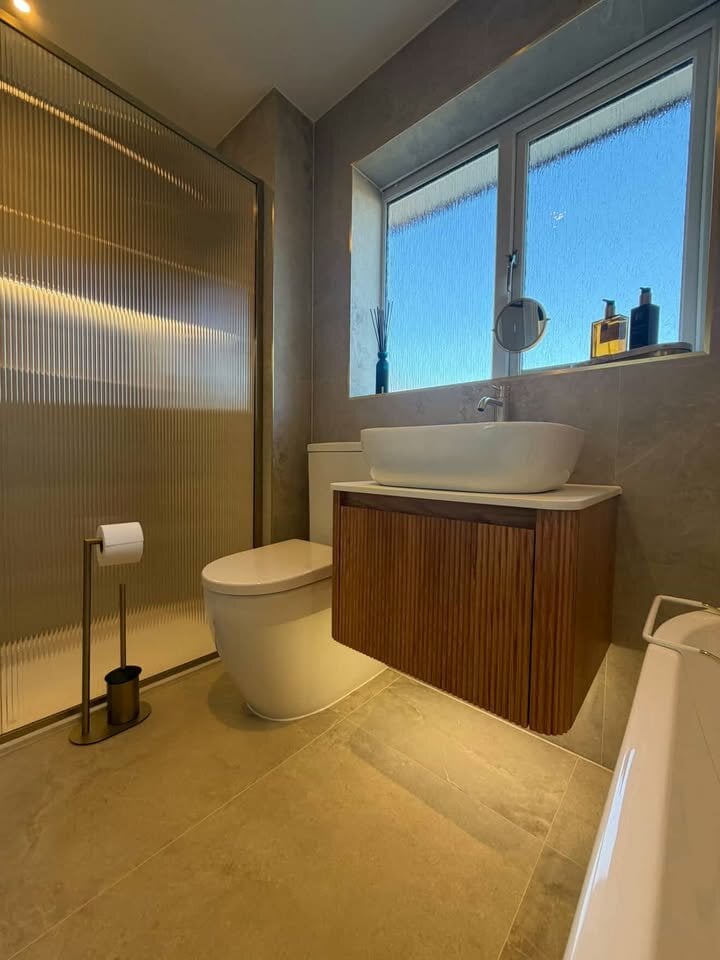 Elegant fluted wood vanity and sleek countertop basin beside a luxurious fluted glass screen and stunning stone tiles.