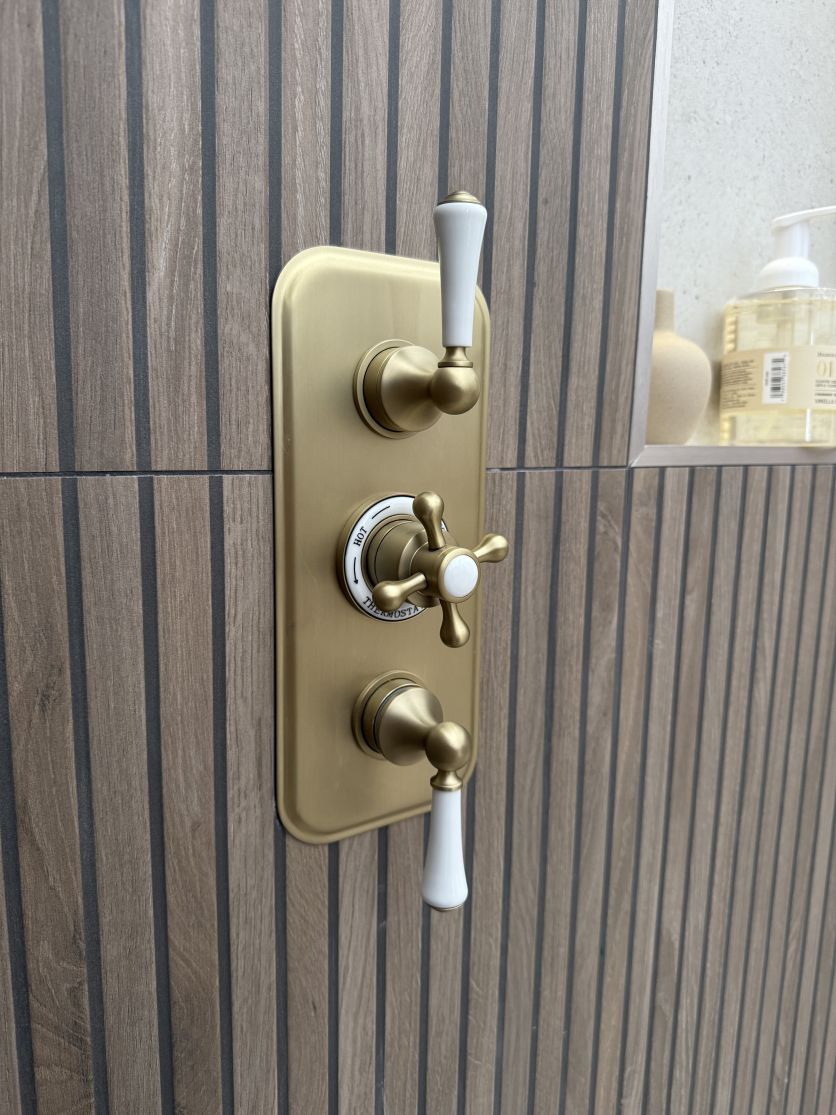 Traditional Warwick brushed gold triple shower valve installed on textured Ottoman wood slat tiles beside a shower niche.