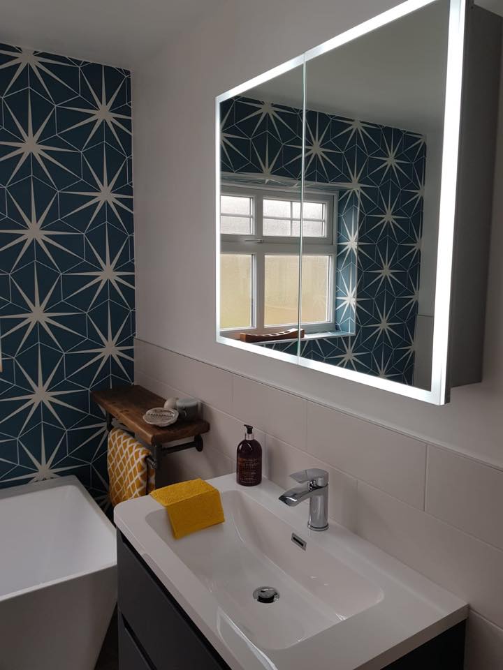 A modern dark grey vanity unit with a white ceramic basin and chrome mixer tap, positioned below a large LED illuminated mirror cabinet against a striking blue and white star-patterned geometric feature wall.