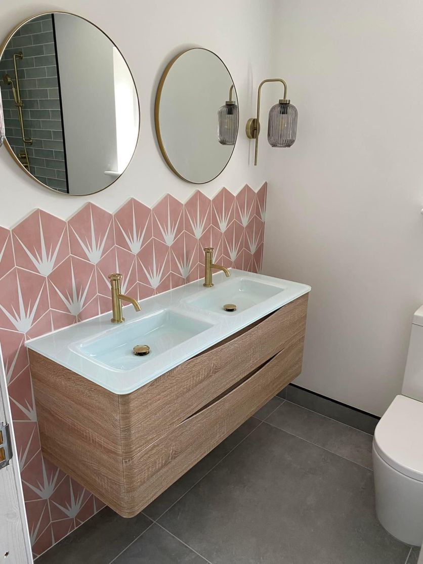 Modern bathroom with pink hexagon tiles, twin light oak vanity, glass basins and brushed gold taps.