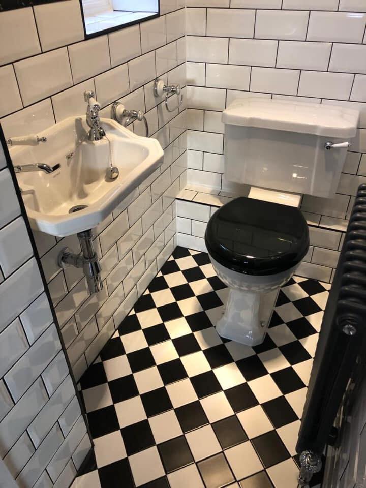 A classic monochrome cloakroom featuring a white ceramic wall-hung basin with traditional chrome crosshead taps, positioned against white bevelled-edge subway wall tiles with dark grout.