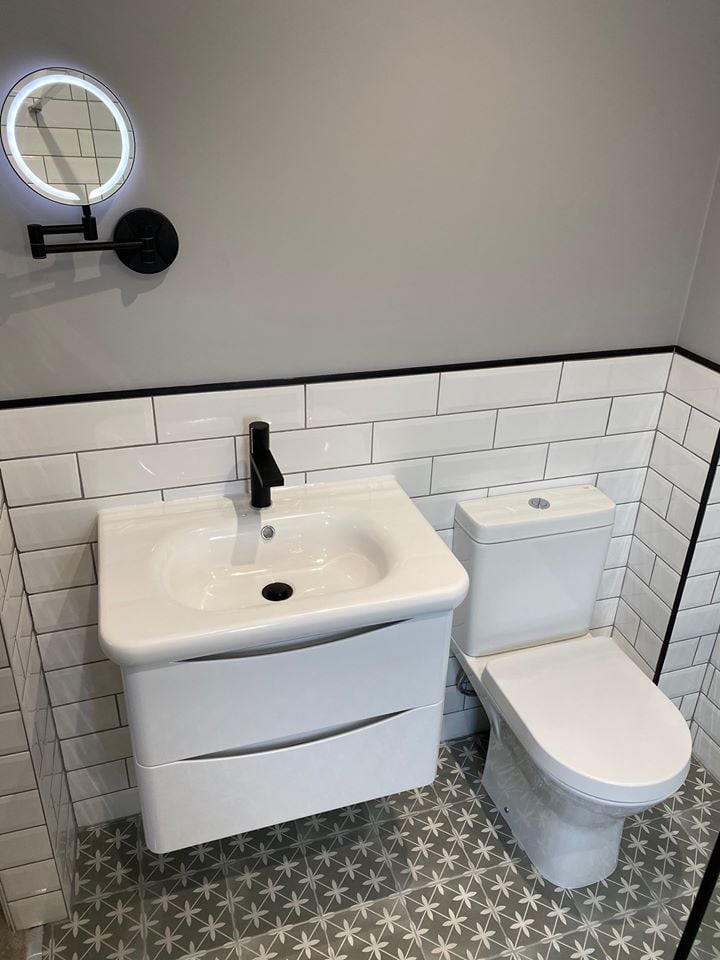 Compact modern bathroom with a white wall-hung vanity, matt black tap, metro wall tiles and grey patterned star-design floor tiles.