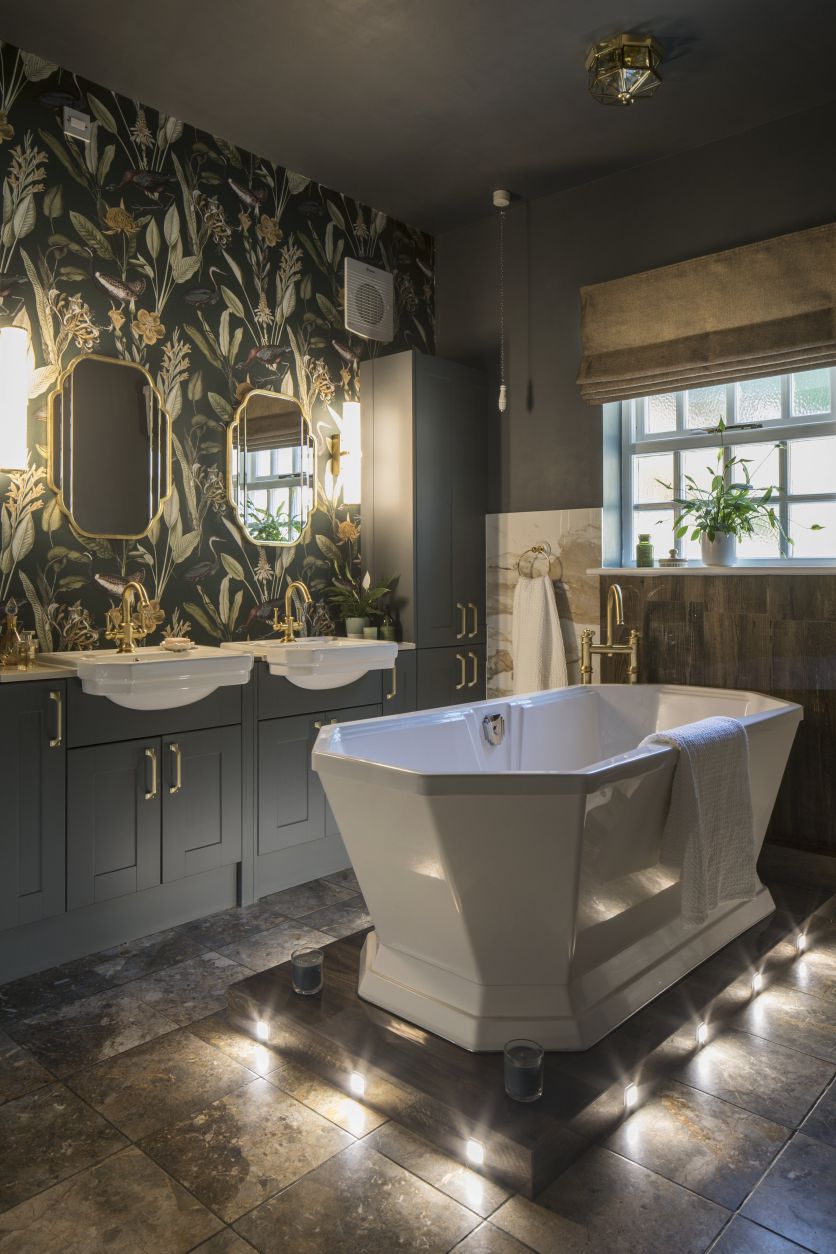 A traditional freestanding bath and dark green double vanity featuring Rainford antique gold brassware.