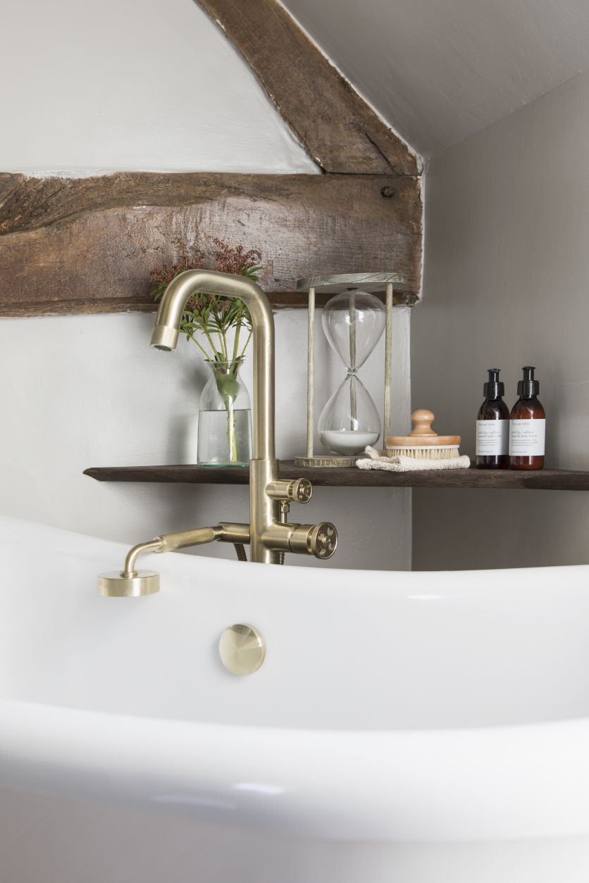 Urban brushed gold freestanding bath shower mixer tap mounted over a traditional white Darcey soaking tub.