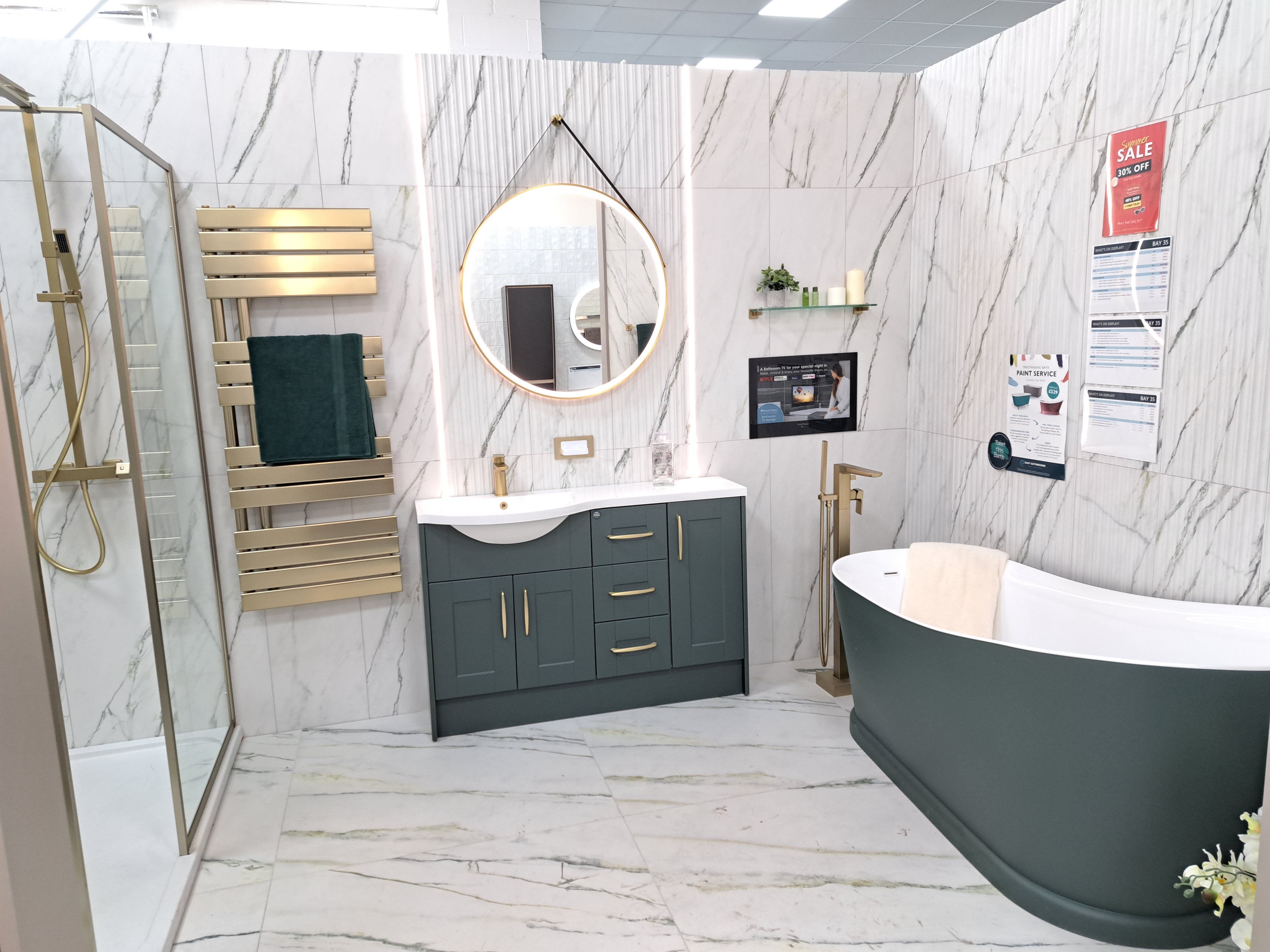 Modern bathroom display with a green vanity unit, freestanding bath and coordinating wall and floor tiles.