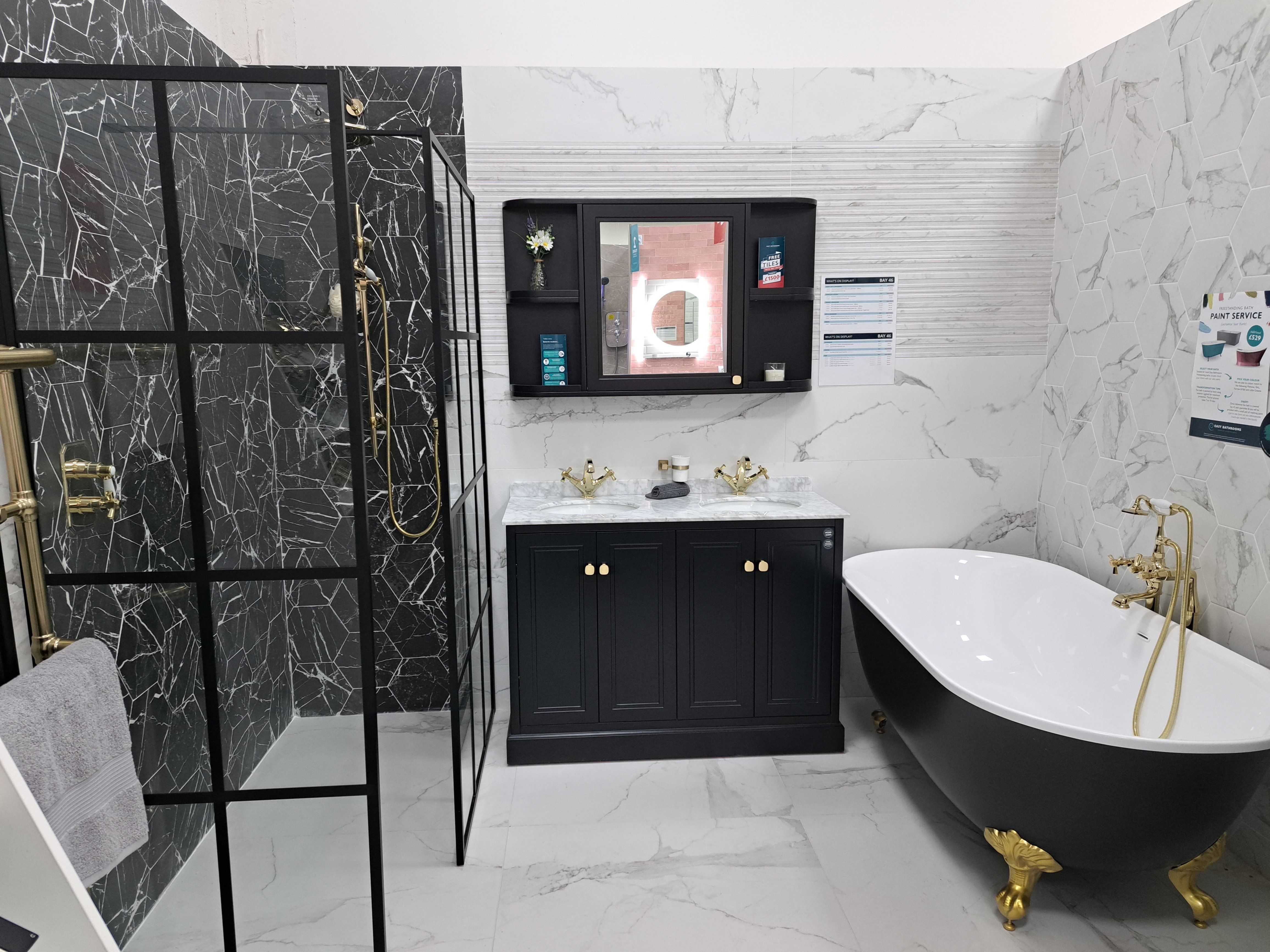 Contemporary bathroom display with black furniture, a freestanding bath and marble-effect wall tiles.