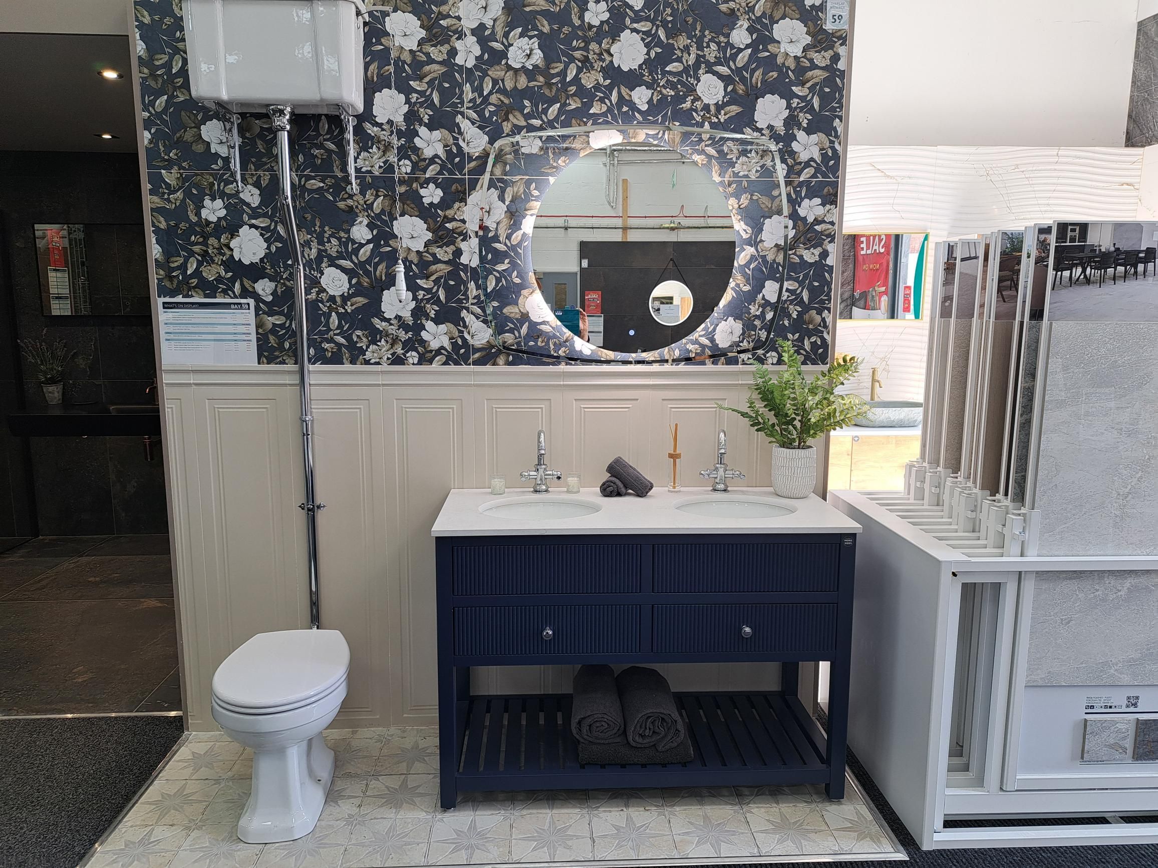 Navy bathroom furniture display with a white basin, round mirror and patterned feature tiles.