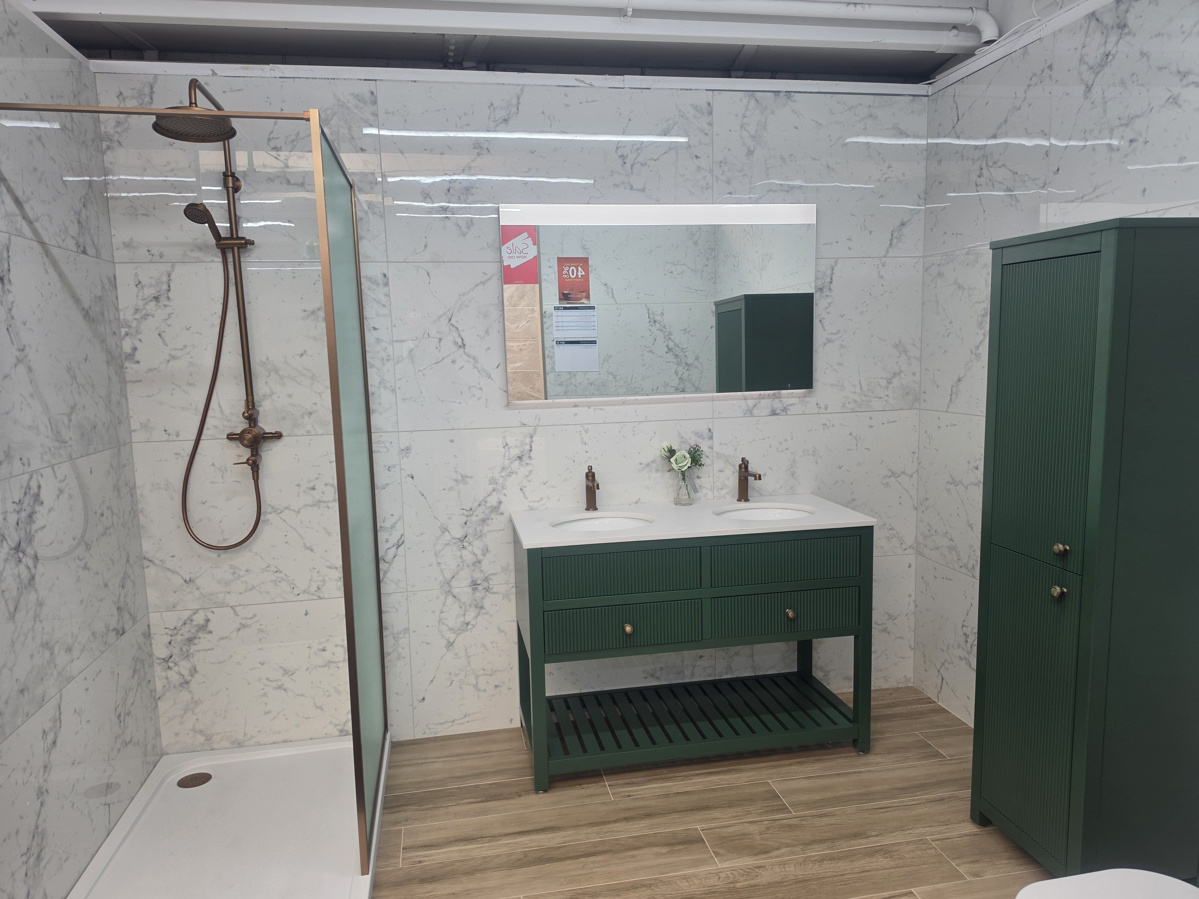 Bathroom showroom display featuring modern emerald green bathroom furniture and brushed bronze shower and hardware