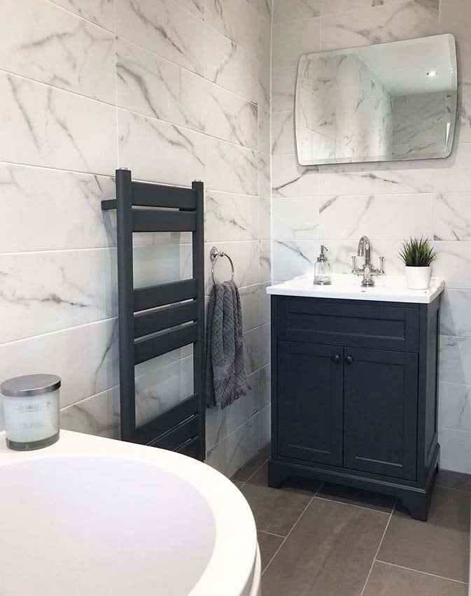 Traditional grey bathroom with marble wall tiles, grey vanity, chrome basin tap and heated towel rail.