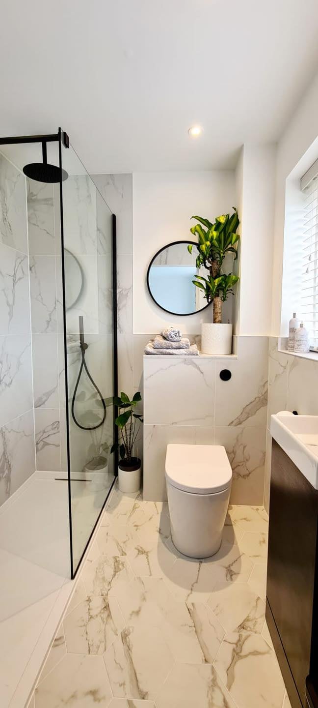 Modern bathroom with marble tiles, black walk-in shower, rimless toilet and greenery for a clean contemporary look.