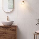 Modern bathroom wall vertically tiled in Kenya Blanco Ceramic Wall Tiles behind a wooden vanity with brass mixer.