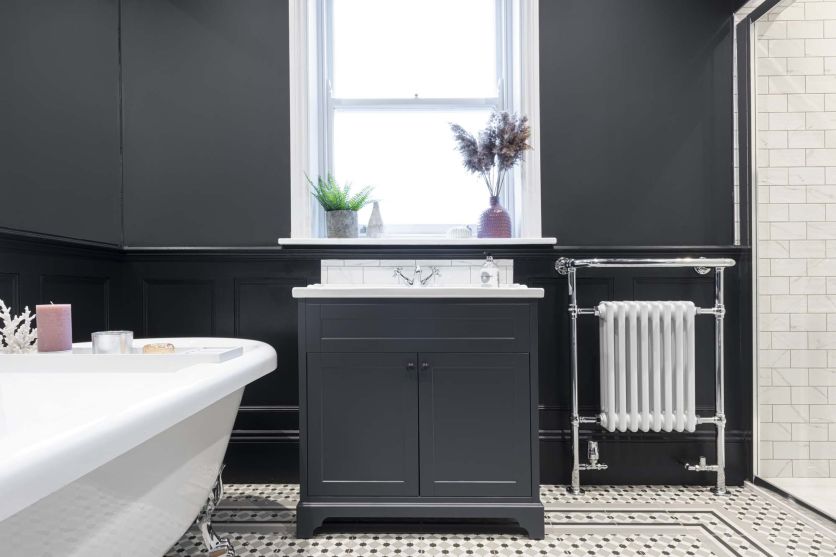 Traditional black and white bathroom with freestanding bath, classic vanity unit, chrome heated towel rail and patterned floor tiles.