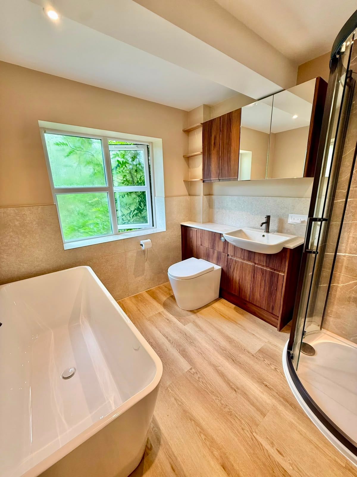 Completed bathroom showing freestanding bath, vanity unit and large window in a bright modern space.