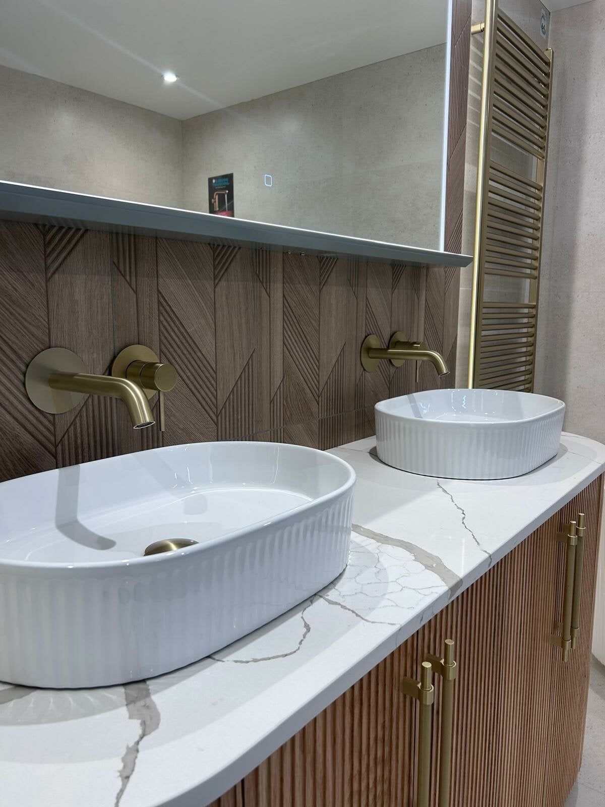Double countertop basin area in the Revel display at Easy Bathrooms Portsmouth with ribbed detailing and warm wood finishes.