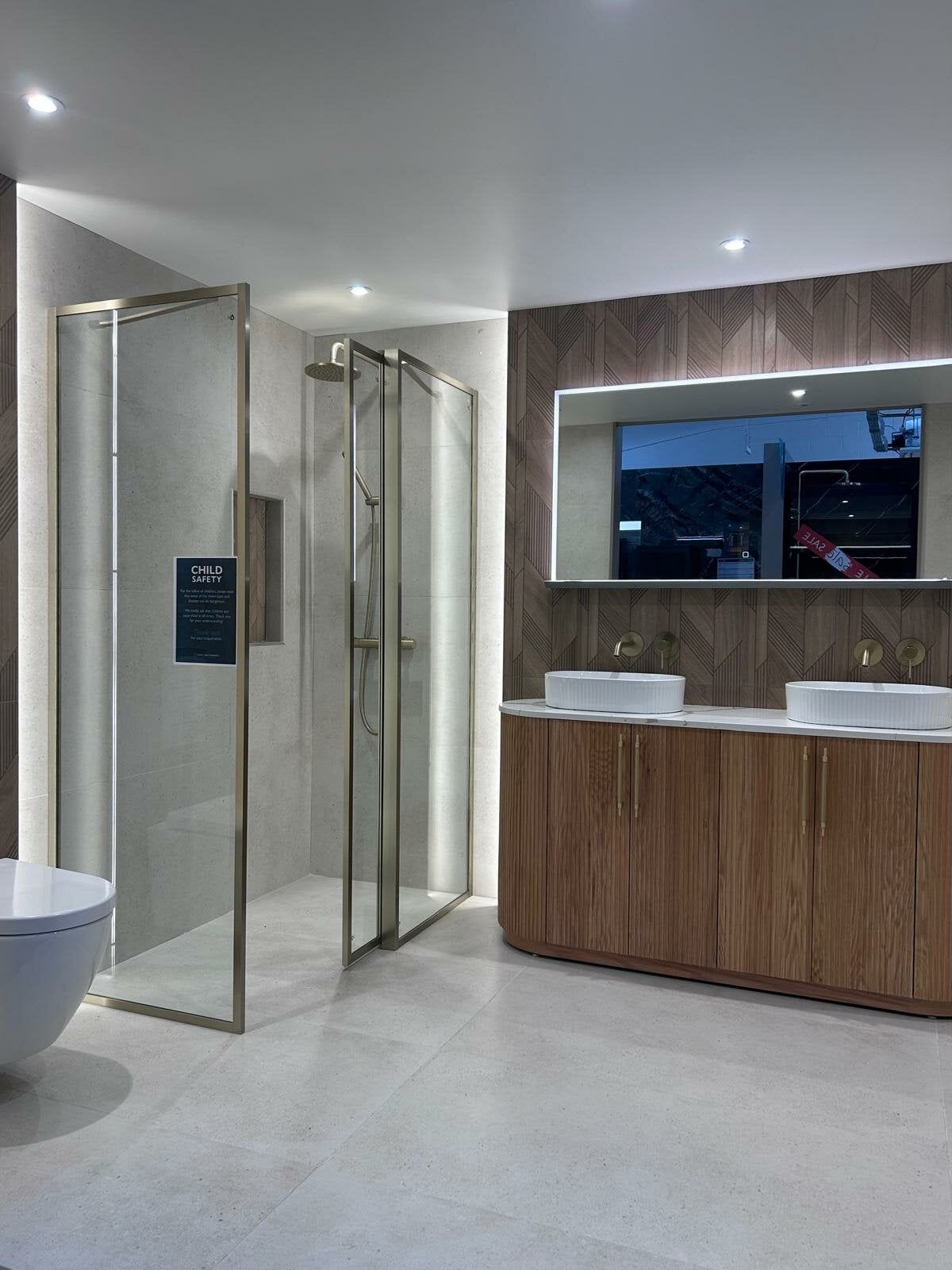 Revel bathroom display at Easy Bathrooms Portsmouth featuring concrete-effect walls, wood-effect furniture and brushed gold brassware.