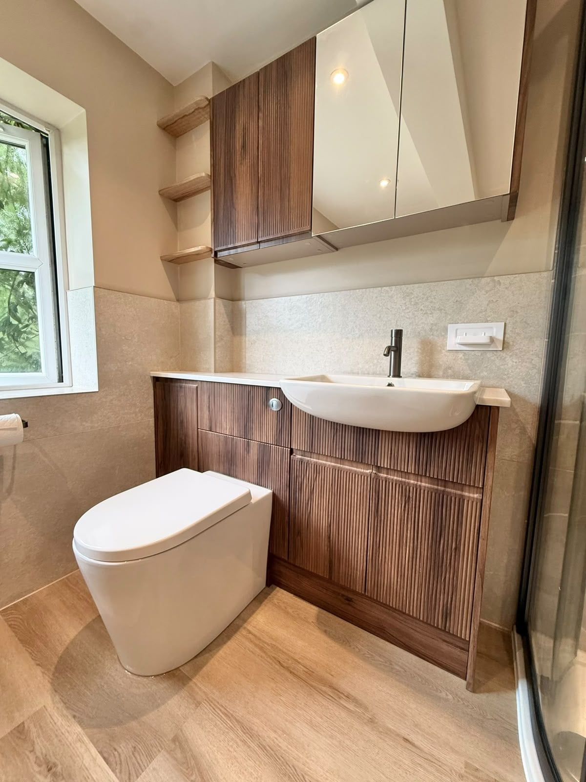Completed bathroom with wood-effect vanity unit, white basin, toilet and warm neutral wall tiles