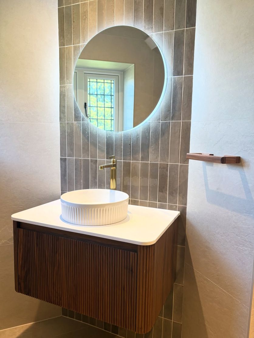 Modern bathroom with ribbed walnut sink, gold tap, round mirror and dark grey porcelain tiles, creating a stylish space