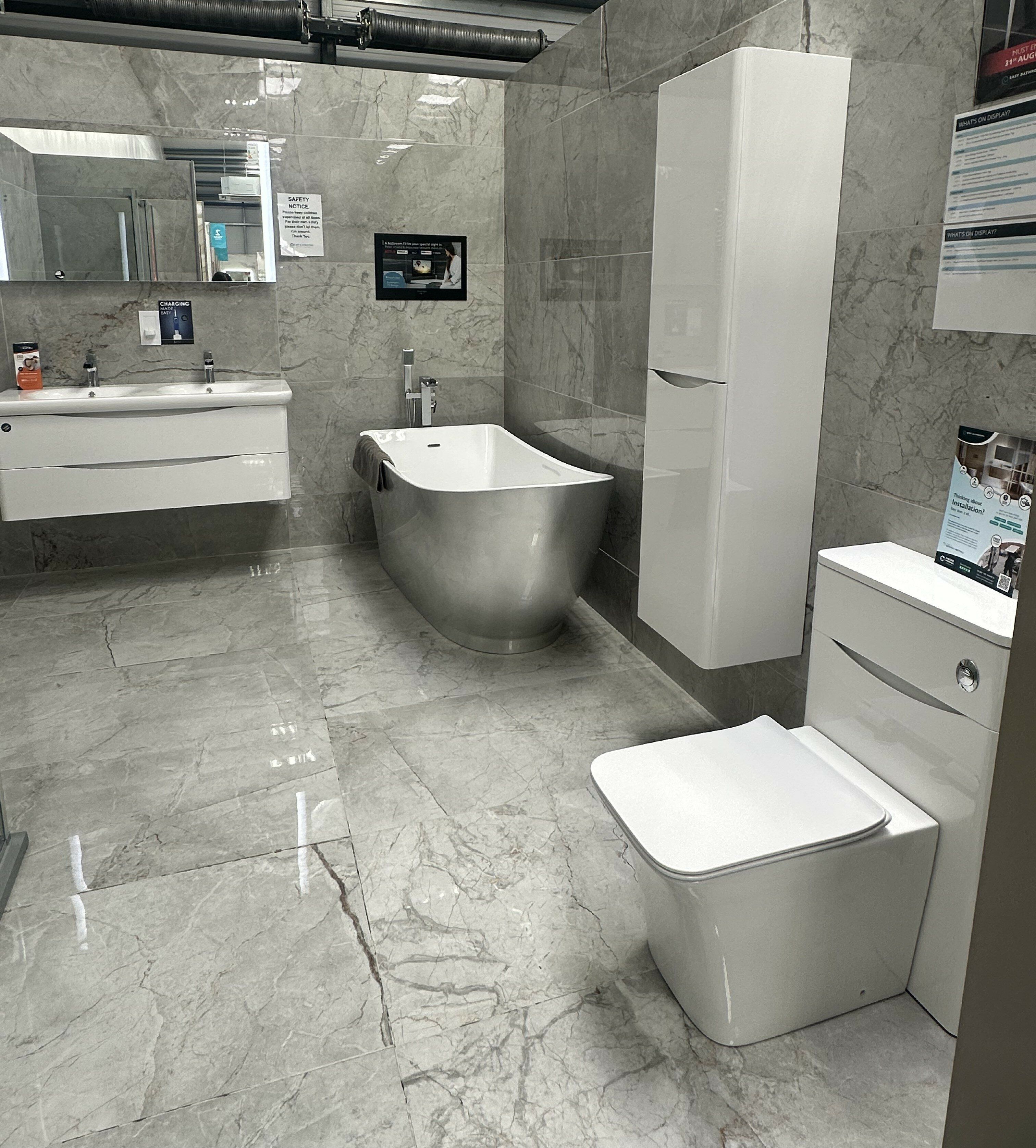 Luxury bathroom display at Easy Bathrooms Watford featuring a silver freestanding bath, gloss white furniture and grey marble-effect tiles.