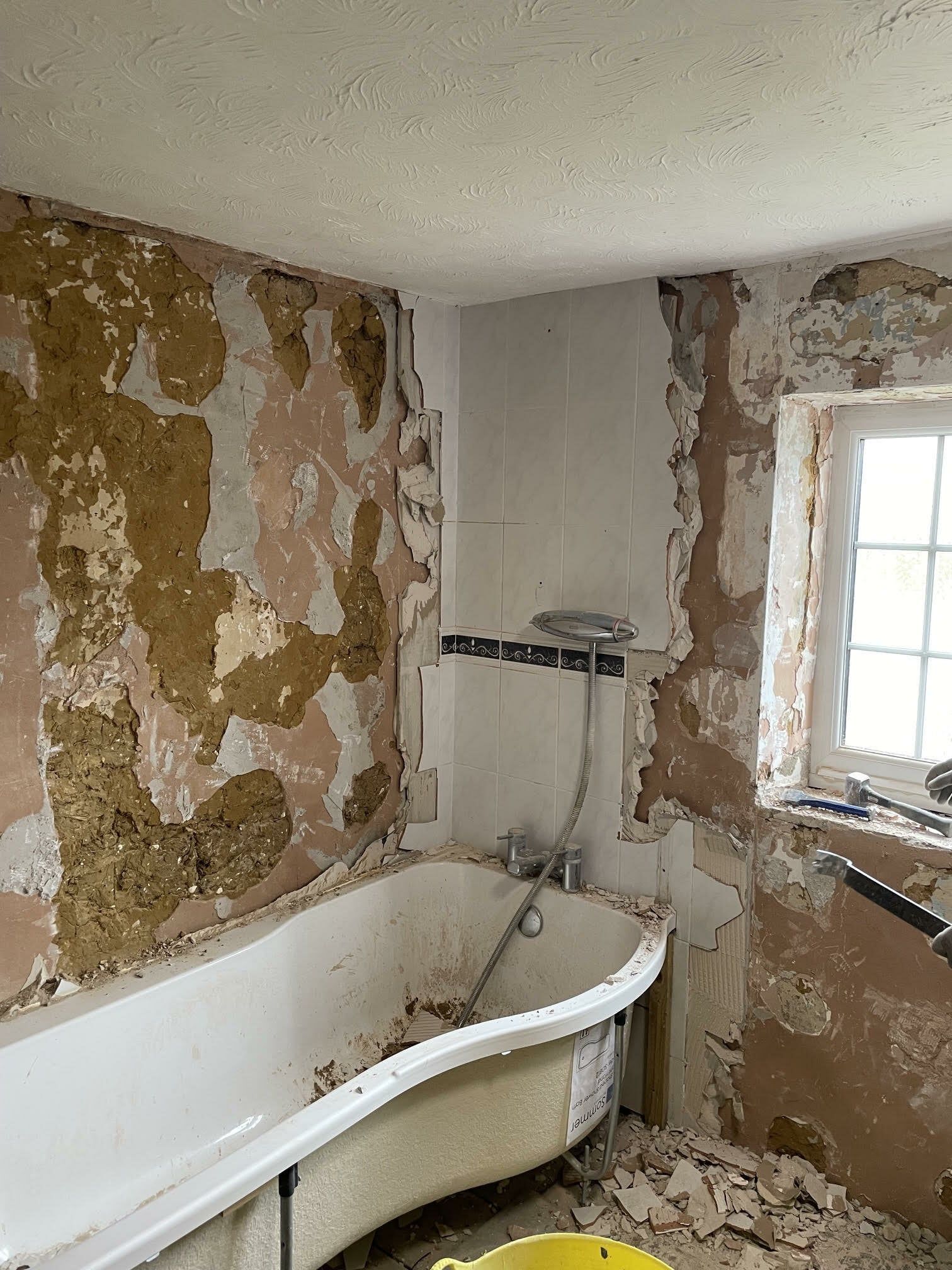 Bathroom before renovation showing an older bath, exposed walls and unfinished surfaces.