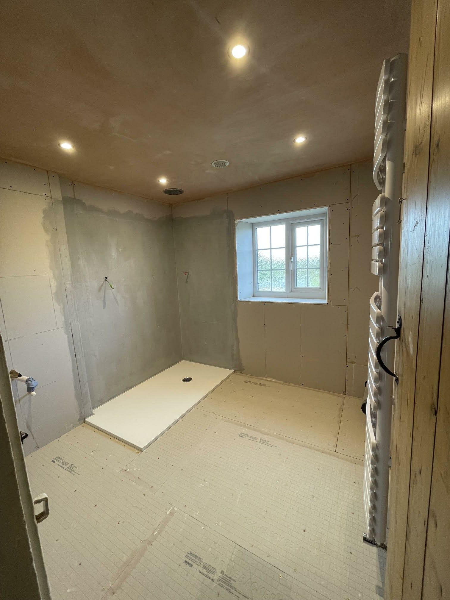 Partially completed bathroom renovation with newly tiled walls, shower tray and neutral floor tiles.