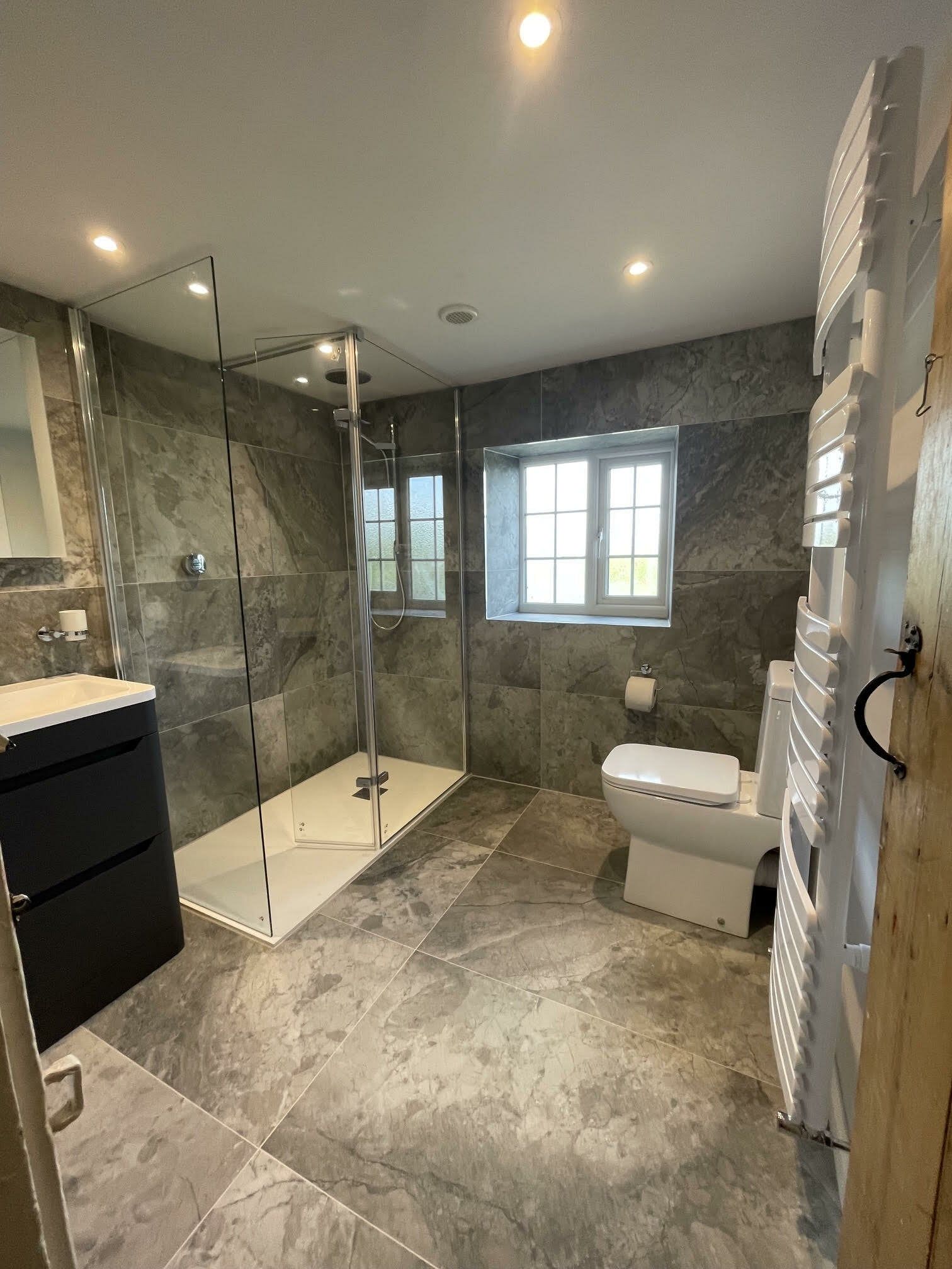 Completed bathroom renovation with neutral stone-effect tiles, walk-in shower, toilet and modern vanity unit.