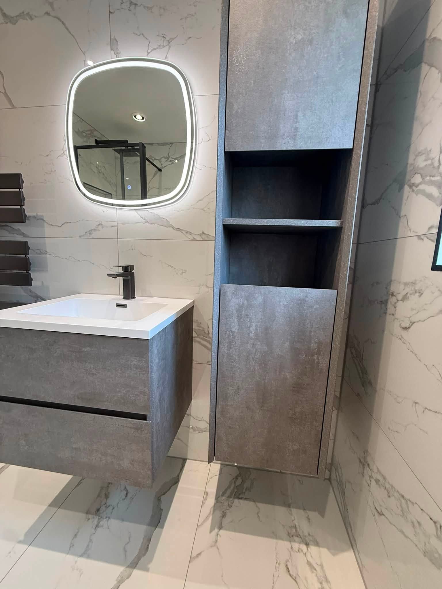 Modern vanity area with illuminated mirror, wall-hung basin unit and tall bathroom storage cabinet.