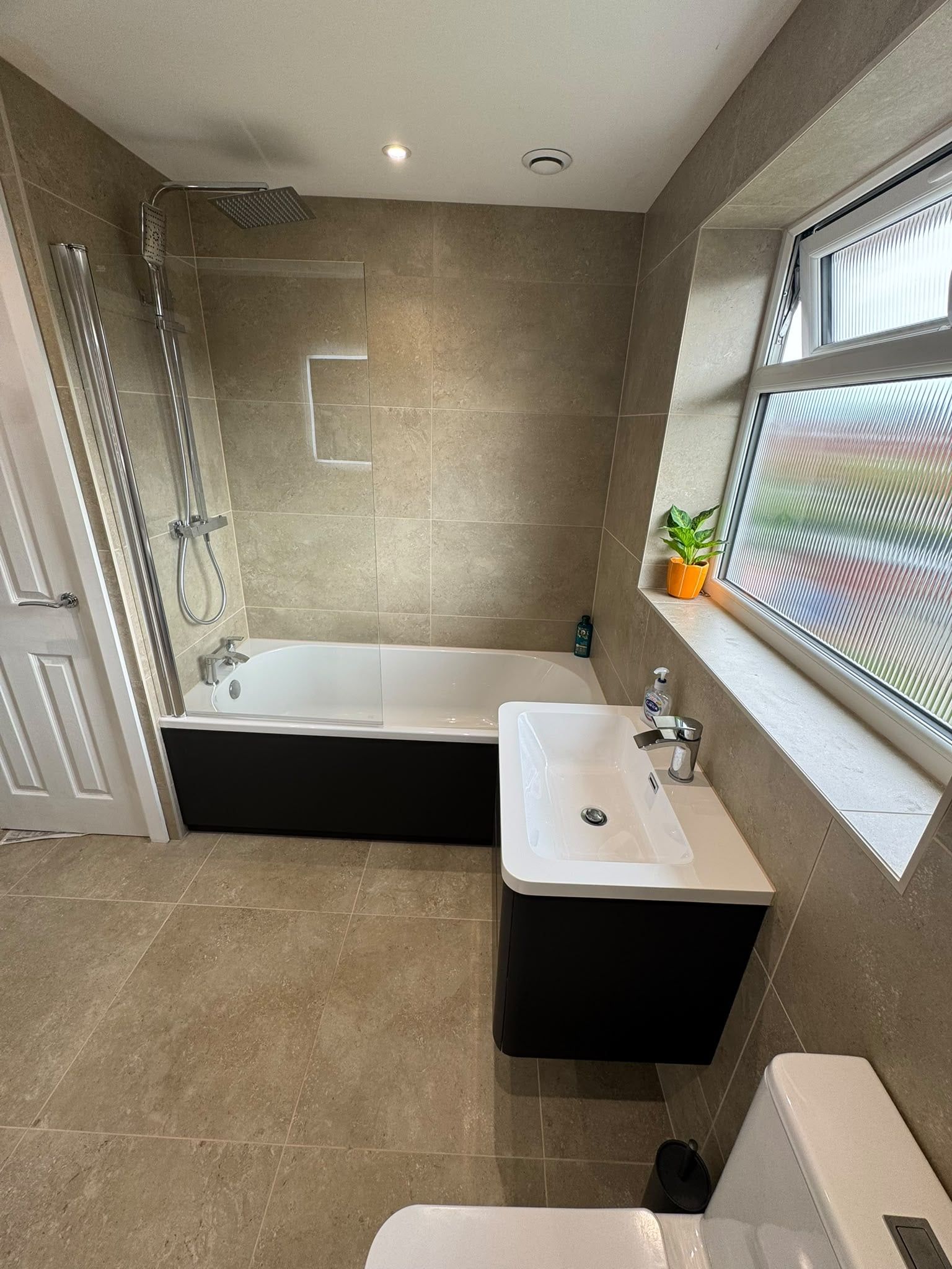 Modern bathroom featuring a white bath, matt black vanity unit and neutral tiled walls and floor.