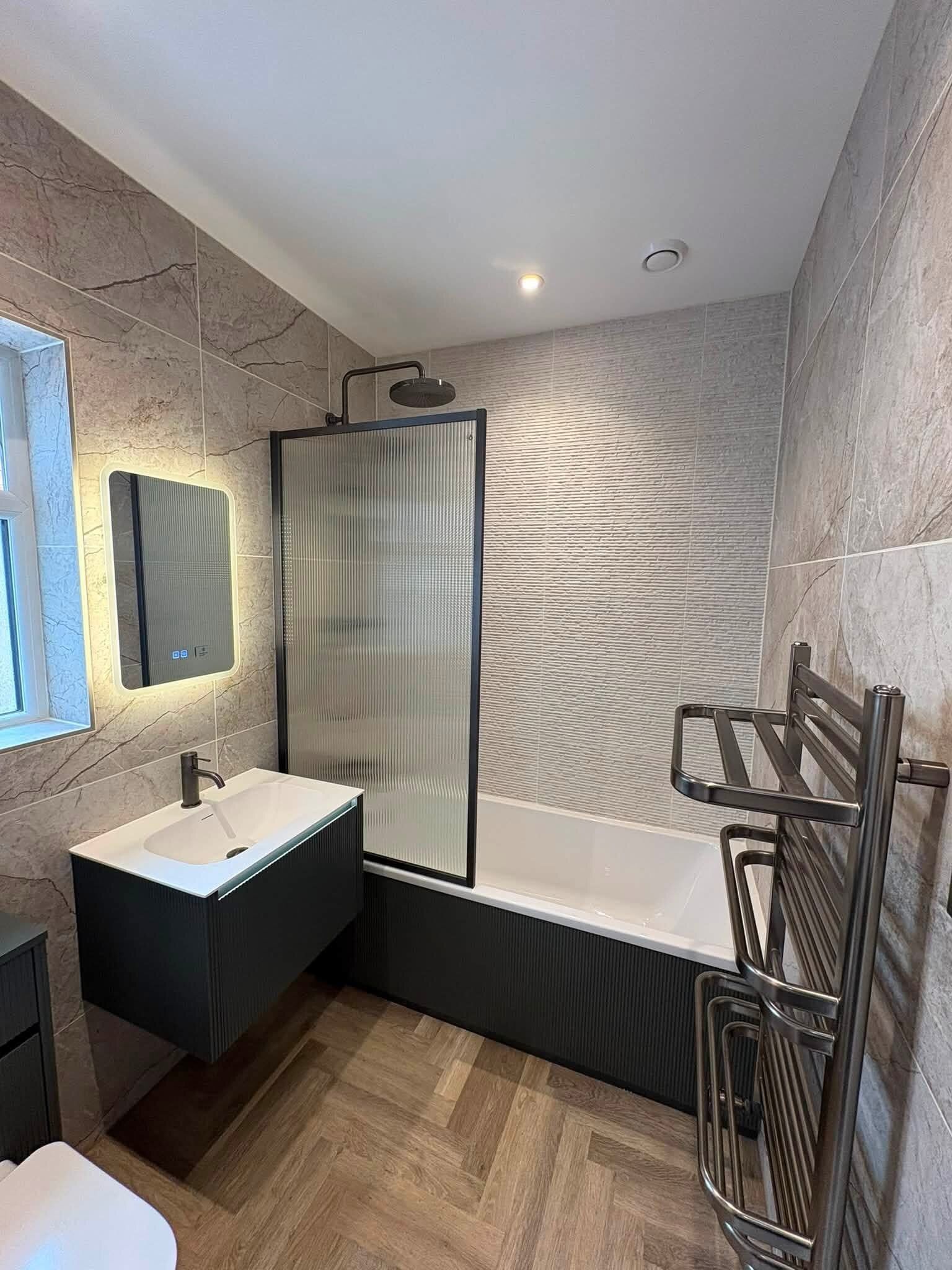 Completed customer bathroom supplied by Easy Bathrooms Portsmouth with warm wood-effect flooring, fluted vanity furniture and black shower fittings.